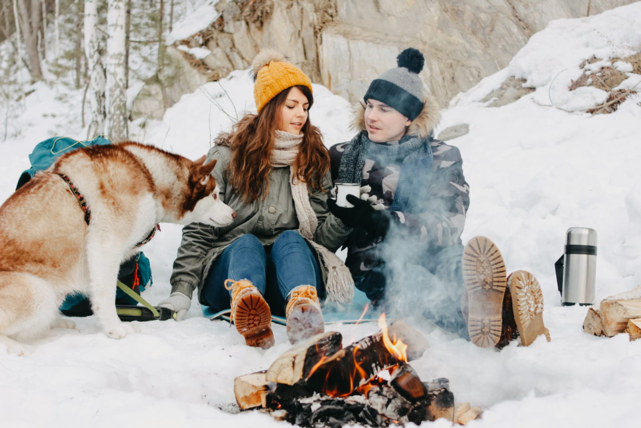Pause im Schnee mit Hund am Lagerfeuer im Winter