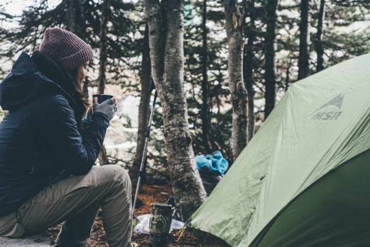 Frau mit Tasse vor dem Zelt im Wald
