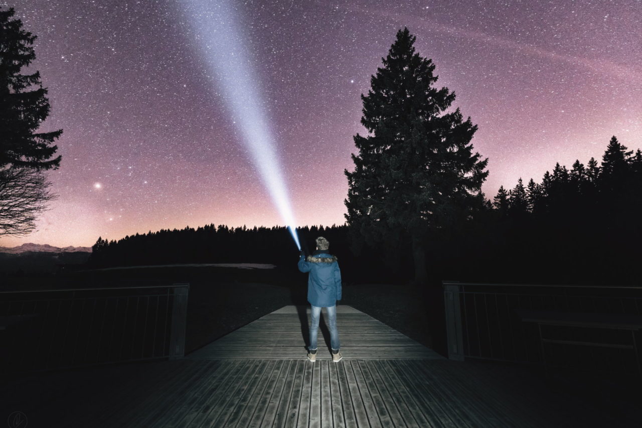 Mann steht mit einer Taschenlampe auf einer Brücke bei Nacht