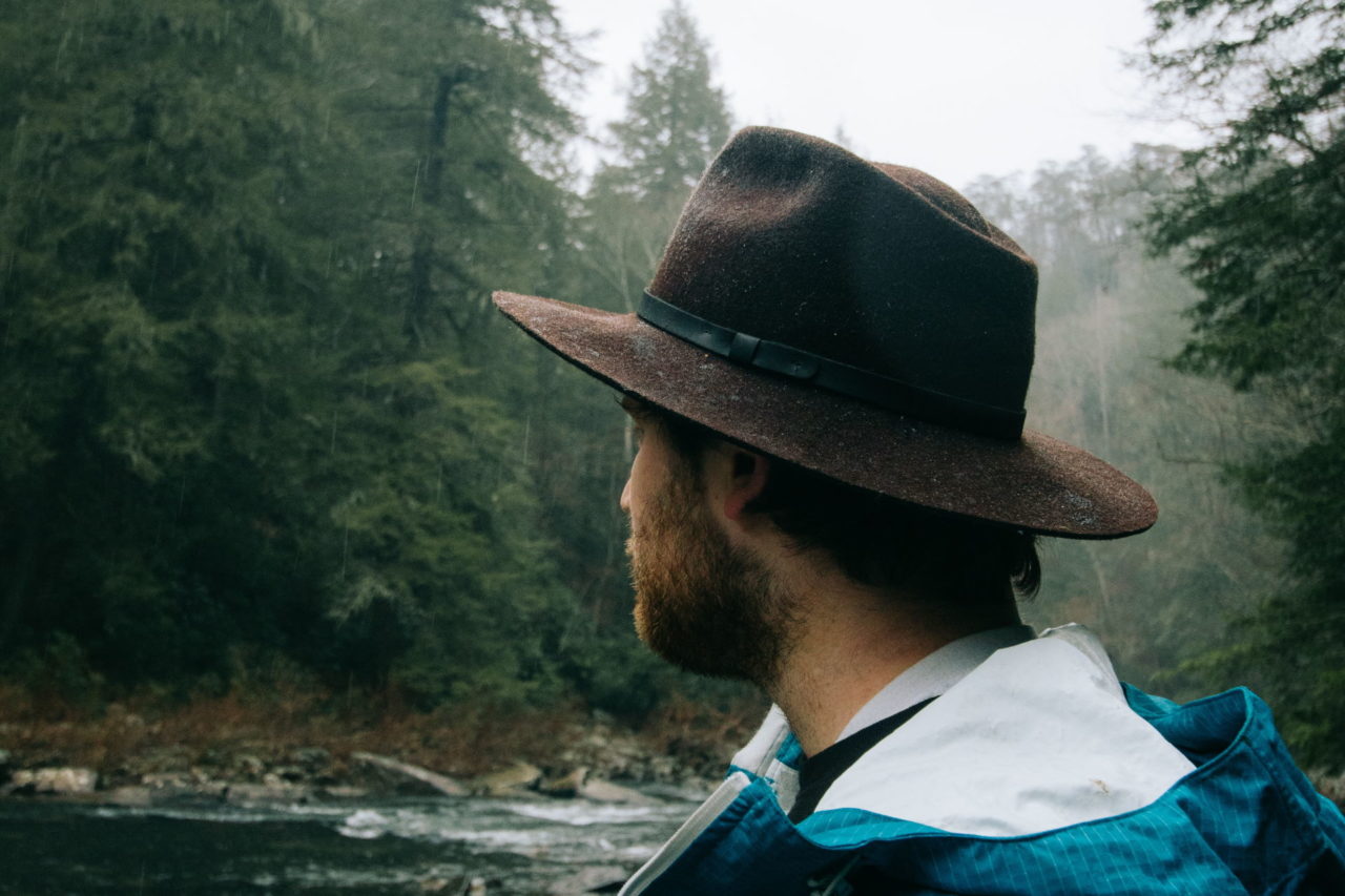 Mann mit Regenjacke und Hut an einem Fluss