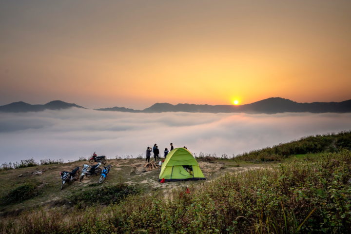 Menschen stehen neben einem grünen Zelt auf einem Bergrücken