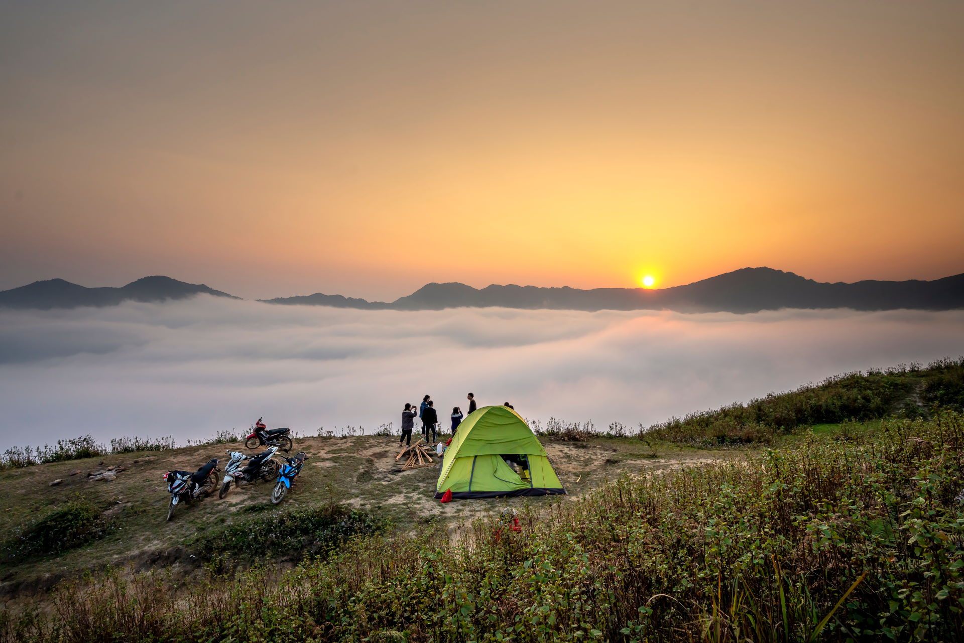 Menschen stehen neben einem grünen Zelt auf einem Bergrücken