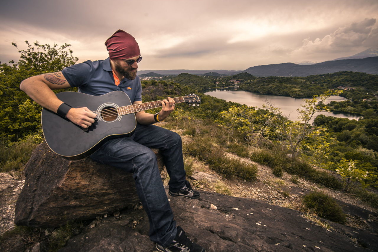Mann Mit Gitarre Sitzt Auf Einem Felsen Am See Und Spielt.jpg
