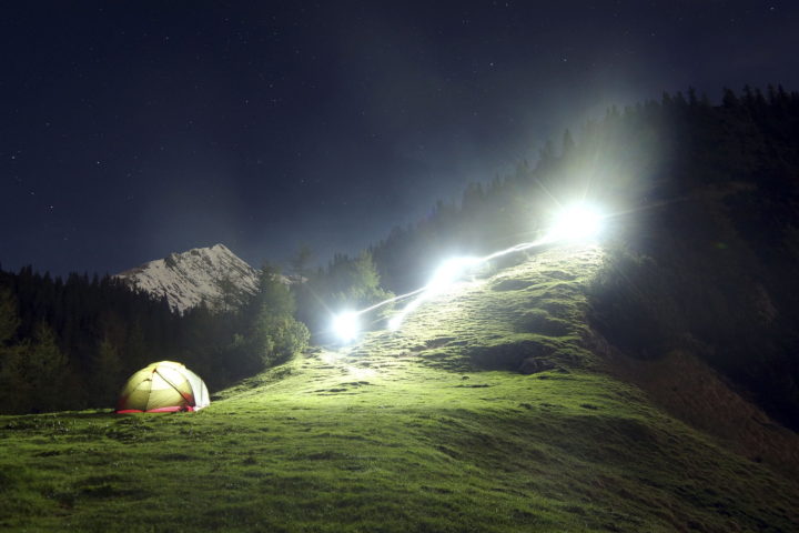 Erleuchtetes Zelt bei Nacht mit großen Scheinwerfern im Gebirge