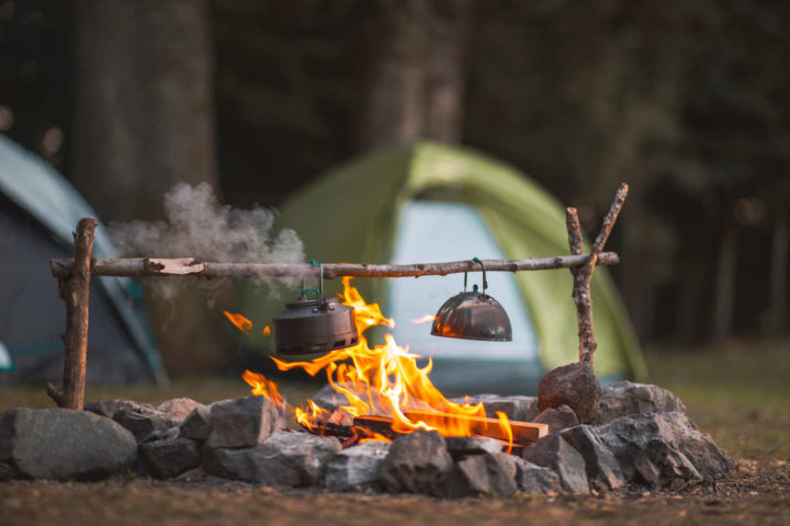 Lagerfeuer und Teekessel mit Kuppelzelt im Hintergrund