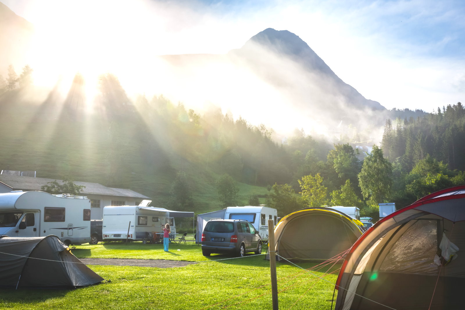 Campingplatz mit Zelten, Stellplatz mit Wohnmobilen, Sonnenstrahlen beim Sonnenaufgang